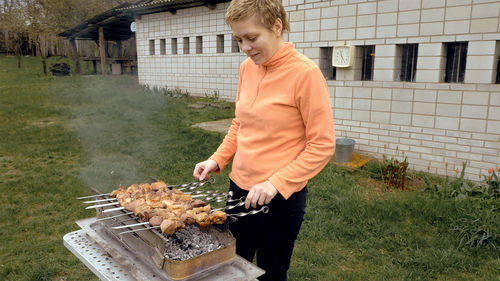 Woman cooking meat on barbecue in yard