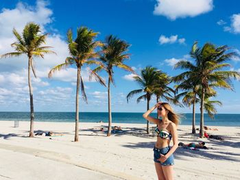Young woman on palm tree at beach against sky