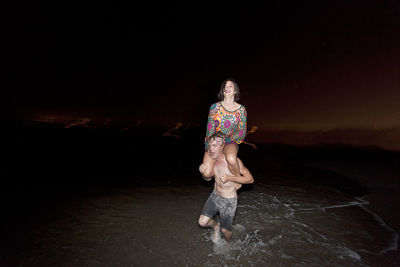 Woman sitting at beach against sky at night