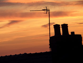 Low angle view of silhouette television antenna and building at sunset