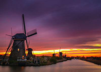 Traditional windmills by river against cloudy sky at kinderdijk