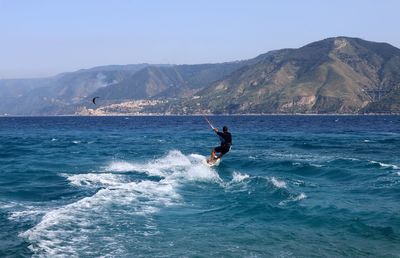 Man surfing in sea against mountain range