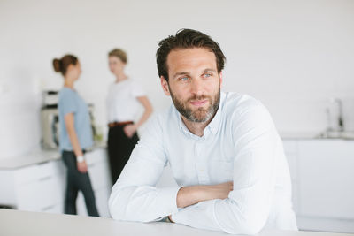 Mid adult man in office, people on background
