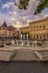 Fountain by swimming pool in city against sky