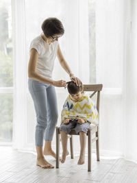 Mother cuts her son's hair by herself. little boy sits, covered with cloth. new normal.