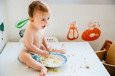 Cute baby girl eating while sitting on table at home