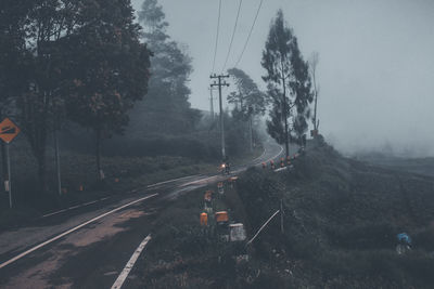 Motorcycle on road by trees against sky during foggy weather