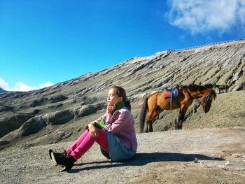 Woman sitting on mountain against sky