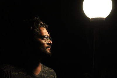 Man looking at illuminated pendant light against black background