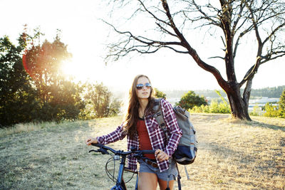 Young woman with bicycle and backpack walking on field