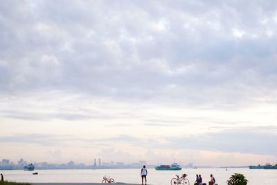 People on beach against cloudy sky