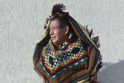 Senior man wearing poncho looking away in front of gray wall