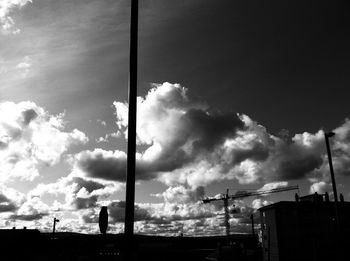 Low angle view of silhouette crane by building against sky