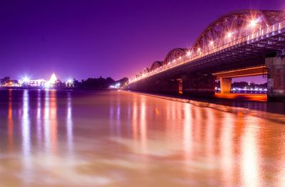 Illuminated bridge over river against sky at night