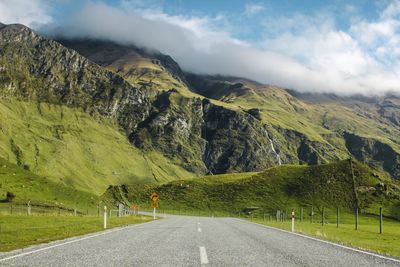 Empty road leading towards mountains against sky