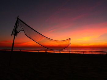 Silhouette volleyball net at beach against orange sky