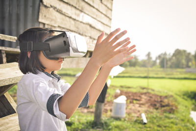 Girl wearing virtual reality simulator at field against sky