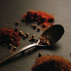Close-up of coriander seeds on spoon amidst spices on table at home