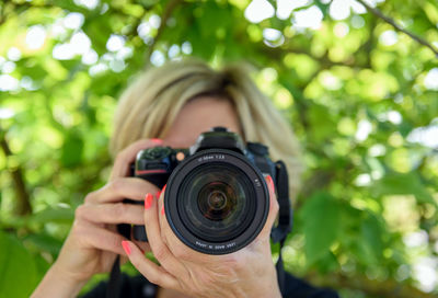 Front view of woman pointing professional digital camera toward viewer