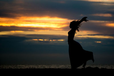 Silhouette woman standing at beach during sunset