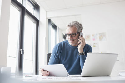 Mature man sitting in office using tablet pc and smart phone