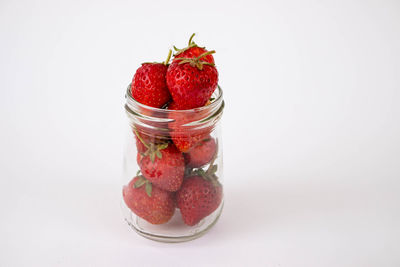 Close-up of strawberries in glass jar against white background