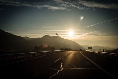 Empty road against mountains at sunset