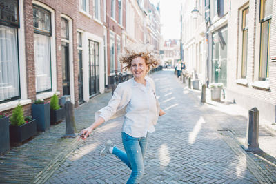 Portrait of smiling young woman on street amidst buildings in city