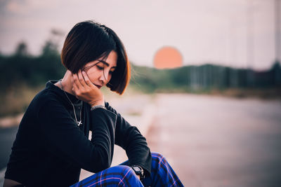 Young woman looking away against sky during sunset