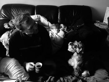 Rear view of woman with dog sitting on sofa at home