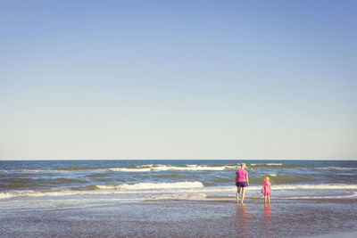 Rear view of grandmother and granddaughter standing in sea against clear sky