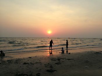 Silhouette family on beach against sky during sunset