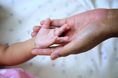 Cropped image of mother holding baby hand on bed at home