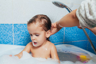 Cropped hand of mother spraying water on daughter in bathroom