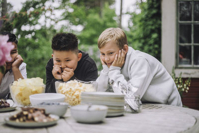 Curious boys leaning on elbows while looking at snacks bowl on table