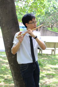 Young man playing the flute next to a tree in the garden