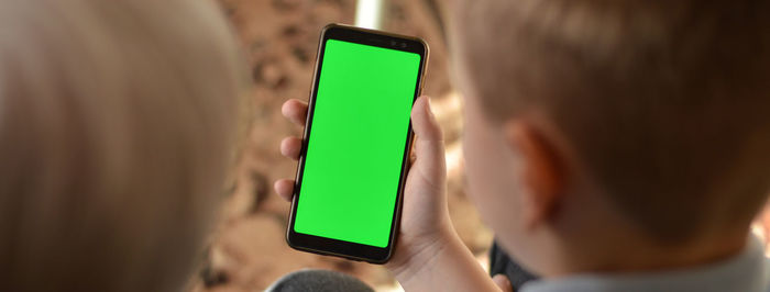 A rear view of a boy and a grandmother who are sitting and looking the green screen of a smartphone.