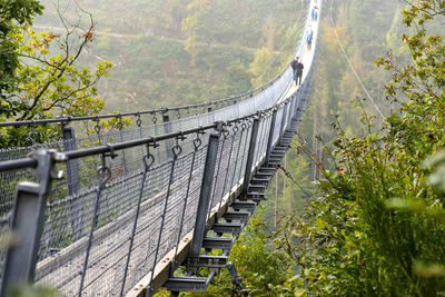 Suspension wooden bridge with steel ropes over a dense forest in west germany, visible tourists. 