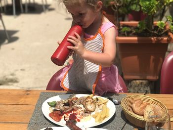 Little girl drinking ketchup from bottle at table