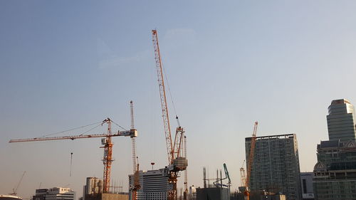 Low angle view of cranes and buildings against sky