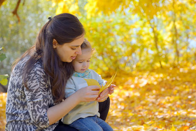 Young woman with daughter holding leaf on field during autumn