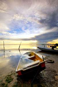 Boat moored on beach against sky during sunset