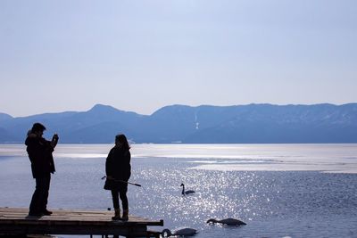 People standing by sea against clear sky