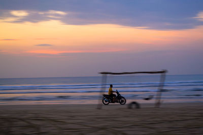 Bicycle on beach against sky during sunset