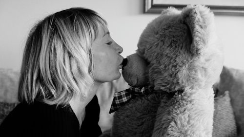 Side view of woman kissing teddy bear at home