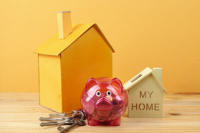Close-up of piggy bank with model homes on table against yellow background