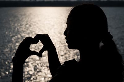 Close-up of silhouette woman gesturing heart shape against sea