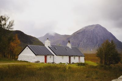 Houses on field by mountains against sky