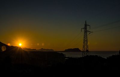 Silhouette electricity pylons on landscape against sky during sunset