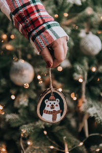 Female hand holding diy wooden handcrafted christmas ornament in front of christmas tree